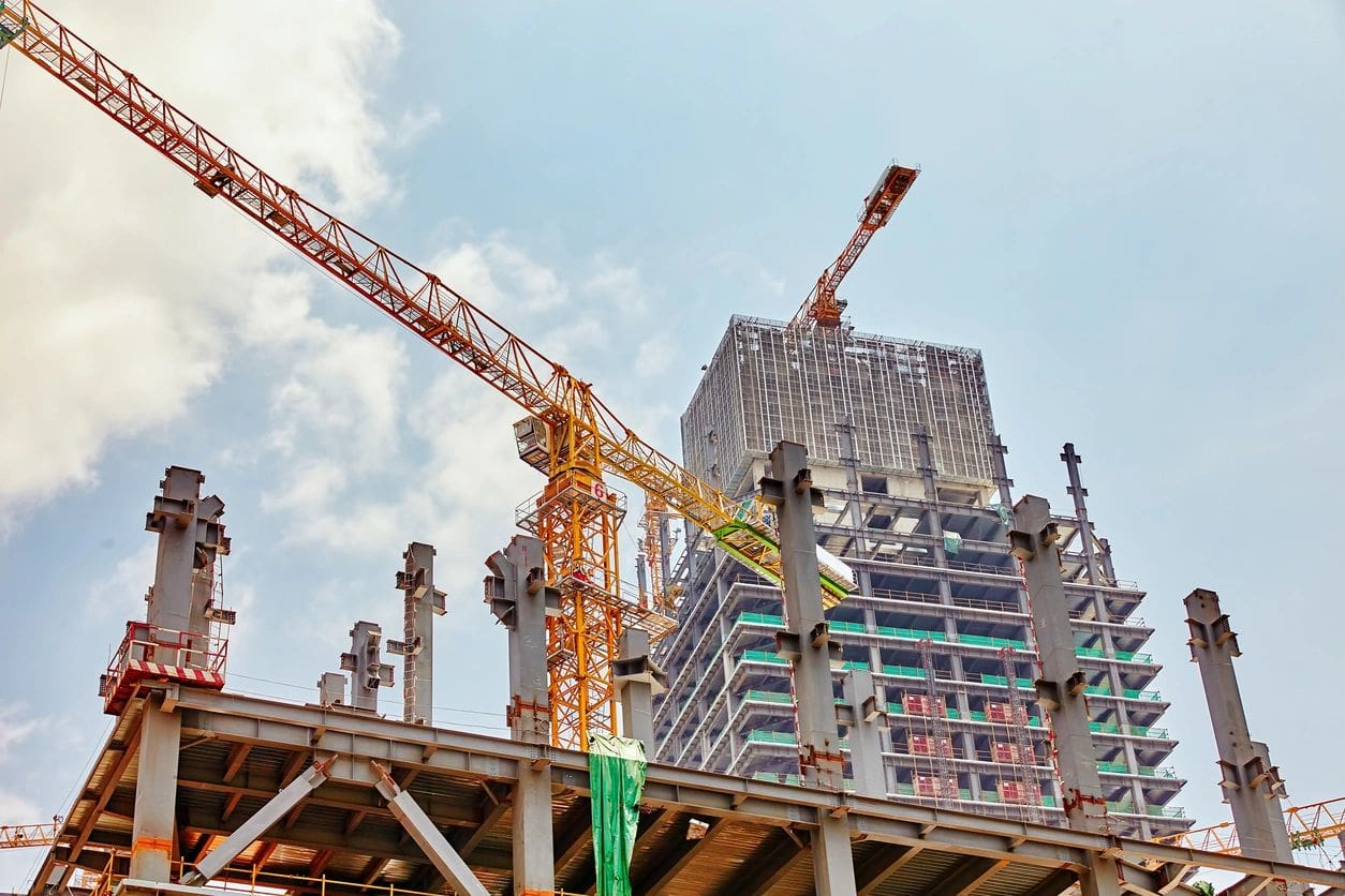 A group of cranes are in front of some buildings.