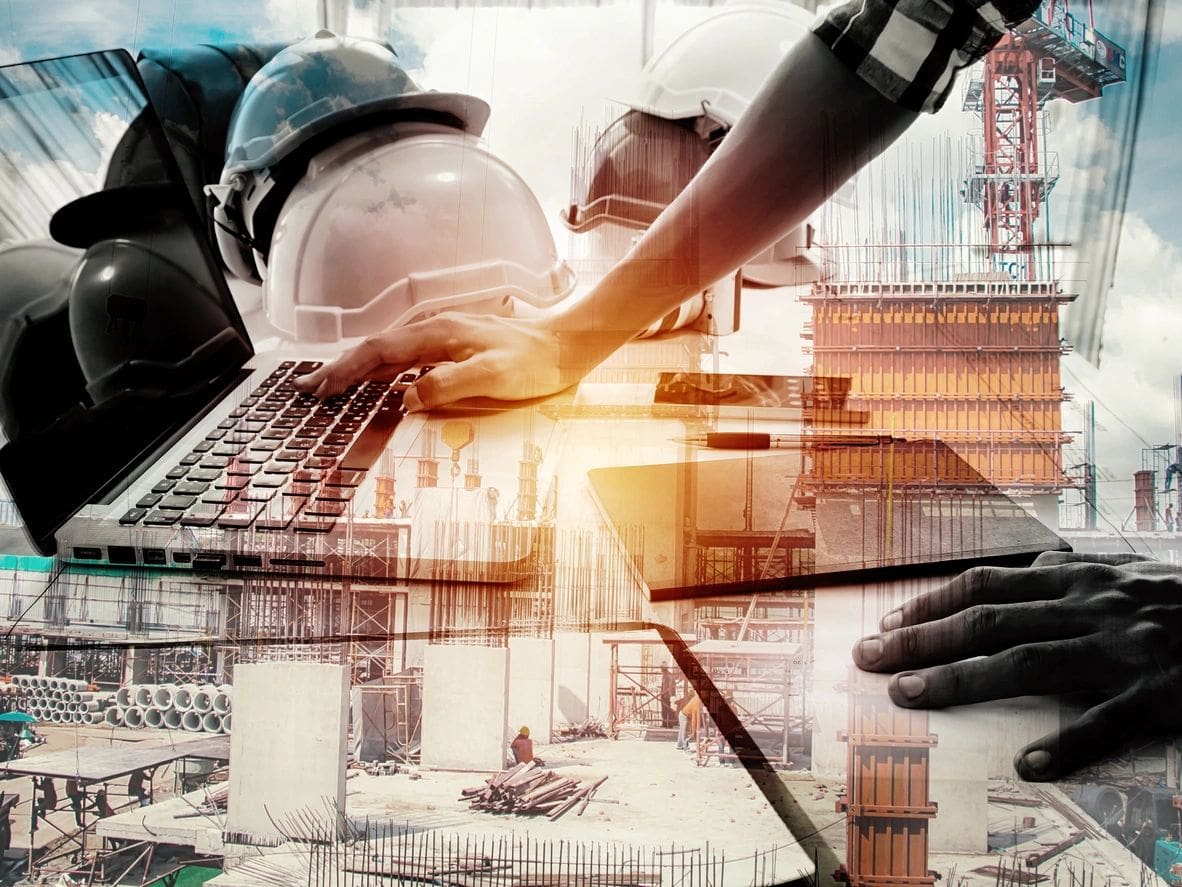 A person with hard hat and keyboard in front of construction site.