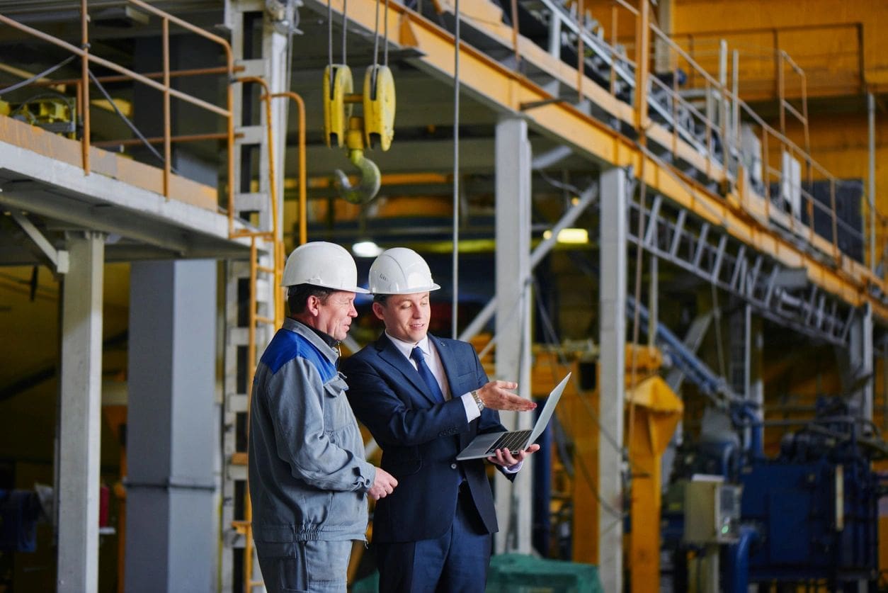 Two men in hard hats and suits are standing next to a building.